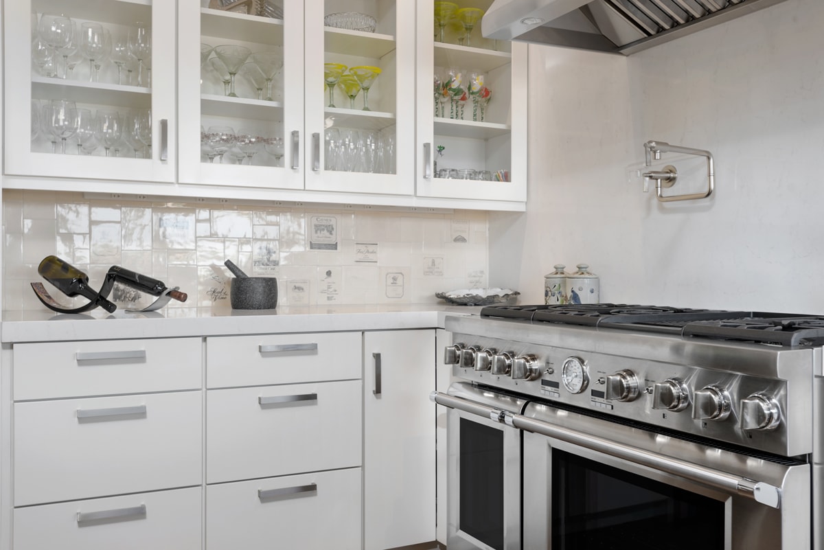 White glass paneled upper cabinetry and closed lower cabinetry with a shiny white tile backsplash.