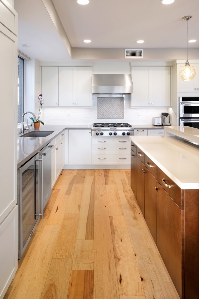 Tall white shaker cabinets with distressed flooring and a warm wood kitchen island.