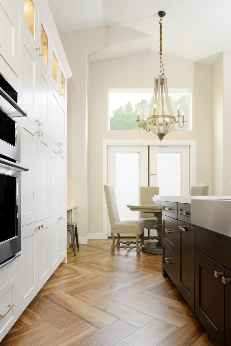 A shot of a kitchen with white and dark brown cabinets looking into a dining room with a table and chandelier.